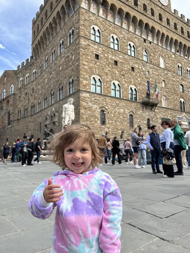 Katherina, souriante, le pouce levé, devant un palais en Italie